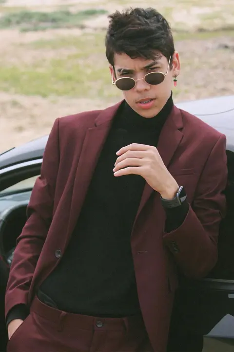 Jayden Croes wearing red suit, black high neck and Apple watch. He is leaning on super car