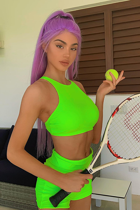 Kristen Hancher beautifully complimenting her purple hair with green sports bikini and shorts while holding ball