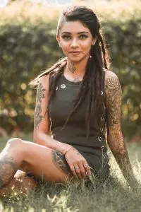Wish Rathod in green dress sitting on grass, showing her tattoos and beautiful smile