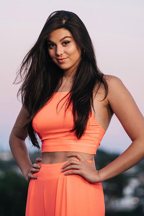 Kira Kosarin is looking at the camera with a smiling face and open hair.