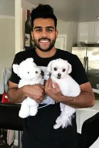 Adam Waheed smiling and have 2 white puppies in hand