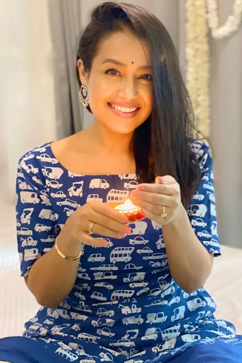 Neha Kakkar in blue dress with candle in hand. looking at camera with stunning smile