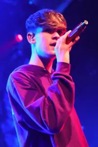 Harvey Mills singing in a concert wearing red hoodie