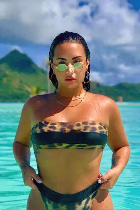 Demi Lovato enjoying and is wet at beach in leapord style top. Her tattoo on wrist complement her perfectly