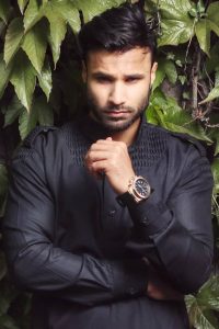 Rahim Pardesi looking intensively at camera and his perfect jaw line can be seen. He is wearing shinny black kurta and black watch