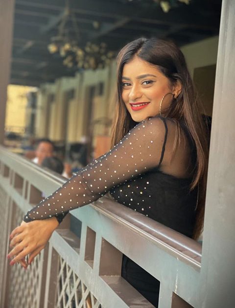 Anam Darbar wearing see through black top and smiling at camera with her perfect red lips and teeth.