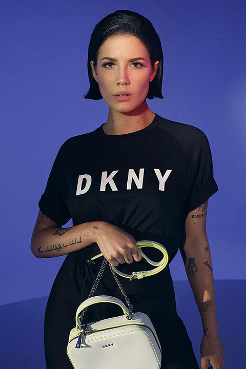 Halsey is holding her bag and posing for a picture in black shirt and trouser.