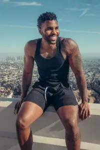 Jason Derulo seating on a wall wearing black vest and black shorts