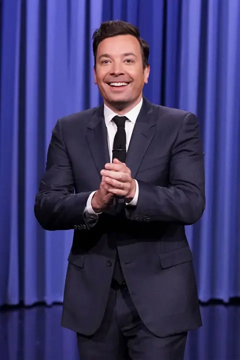 Jimmy Fallon is giving a beautiful smile and wearing dark blue pent coat