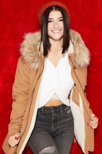 Charli Damelio smiling in white dress and brown coat