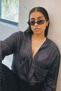 Lilly Singh posing in black dress and shades
