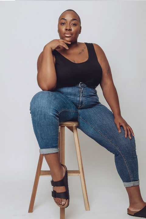 Nyome Nicholas-Williams sitting on stool in black top and blue jeans