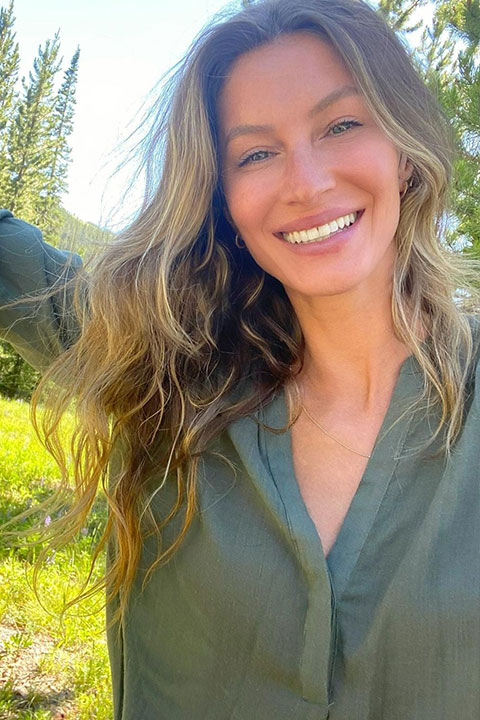Gisele Bundchen is giving smile while looking at the camera and looking beautiful in green shirt.