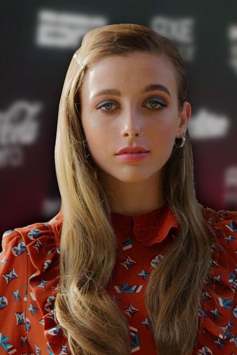 Emma Chamberlain in he exotic look. She has blonde hair and green eyes. She wearing red fashionable dress.
